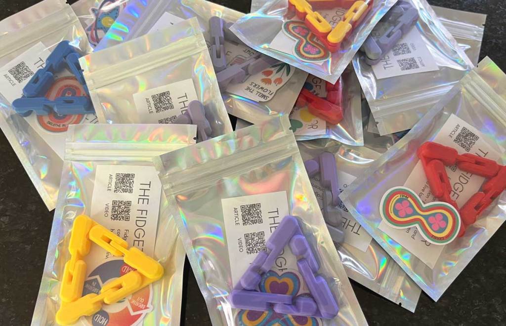 Triangle shaped fidgets in holographic packs. Each fidget pack includes an info sheet and a textured sticker.