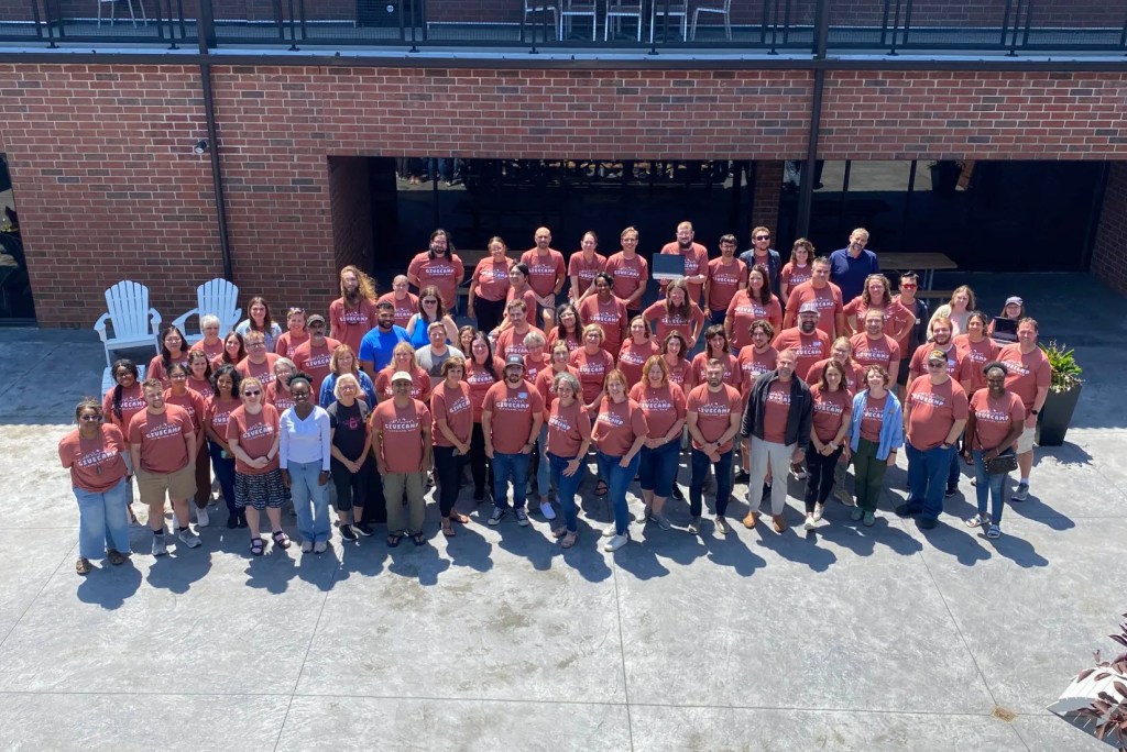 Outdoor group photo of roughly 70 people at the 2024 Cleveland GiveCamp. Most are wearing GiveCamp t-shirts.